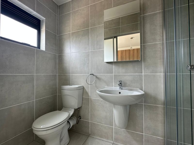 Modern bathroom featuring floor-to-ceiling neutral tiling, a pedestal basin, a wall-mounted mirror cabinet, and a glass-enclosed shower.