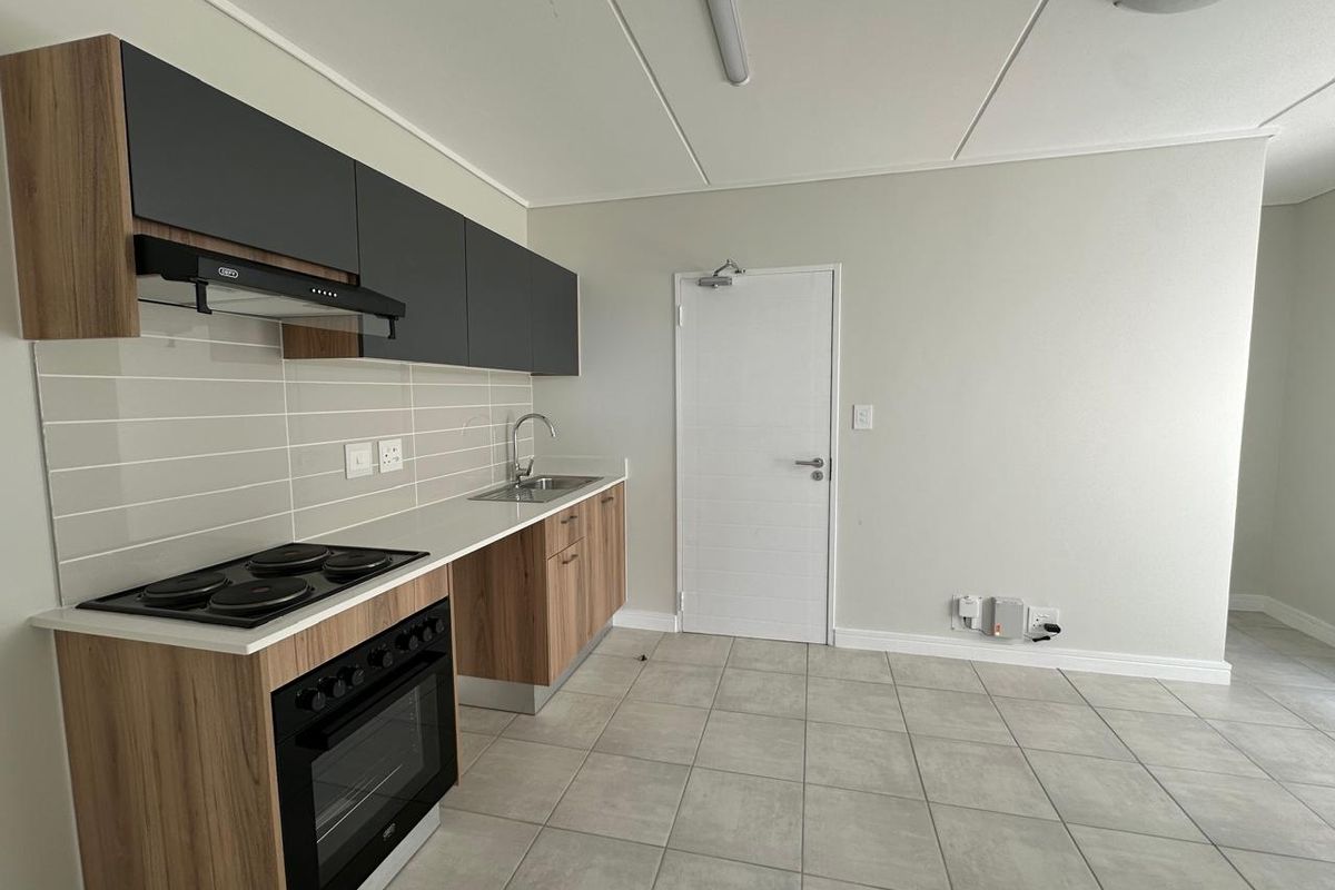 Modern open-plan kitchen featuring wood-grain cabinetry, dark overhead cupboards, built-in oven and hob, and tiled flooring.
