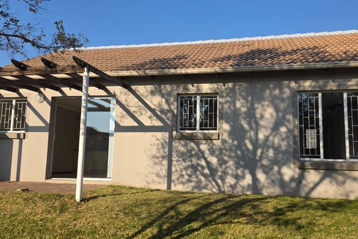Rear exterior view of the townhouse featuring a tiled roof, a timber pergola over a paved patio, and security bars on the windows.