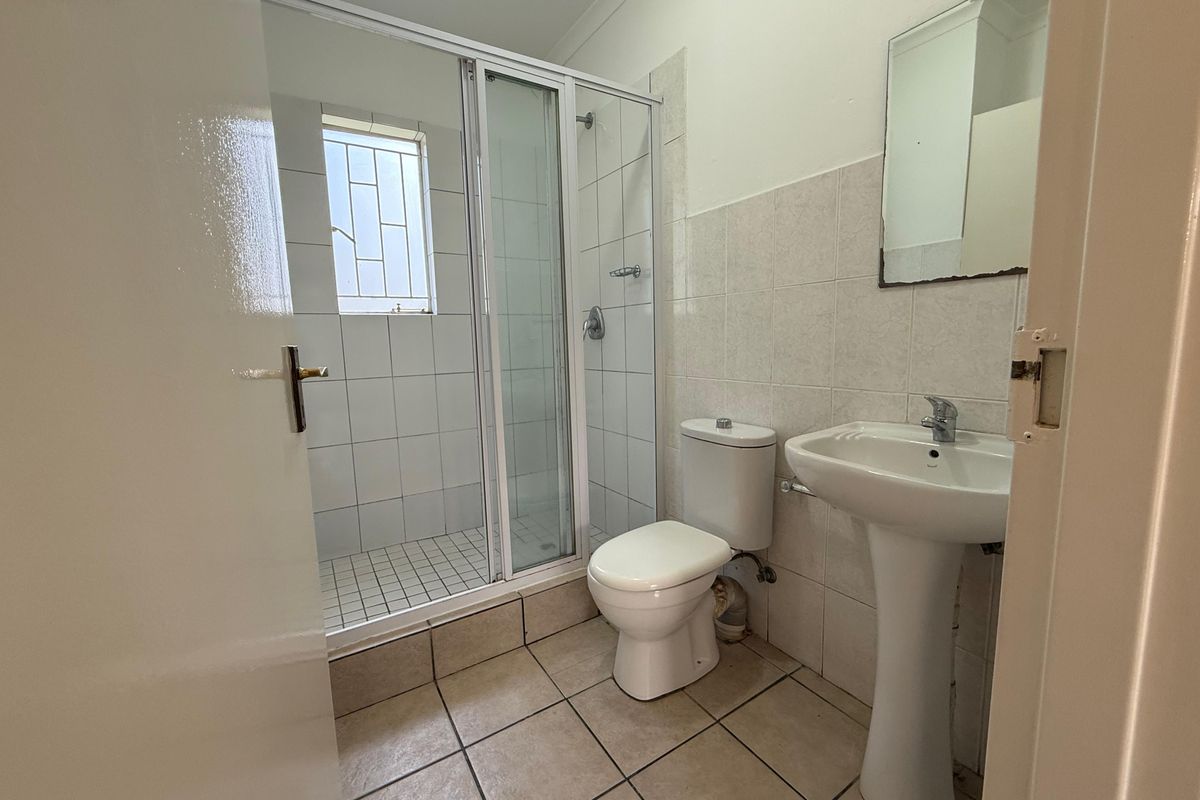 A functional bathroom featuring a glass-enclosed shower, pedestal basin, and toilet with neutral wall and floor tiling.