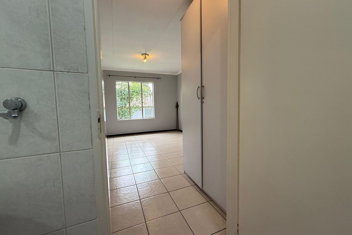 A view from a tiled bathroom doorway looking into a bedroom featuring built-in cupboards and tiled flooring.