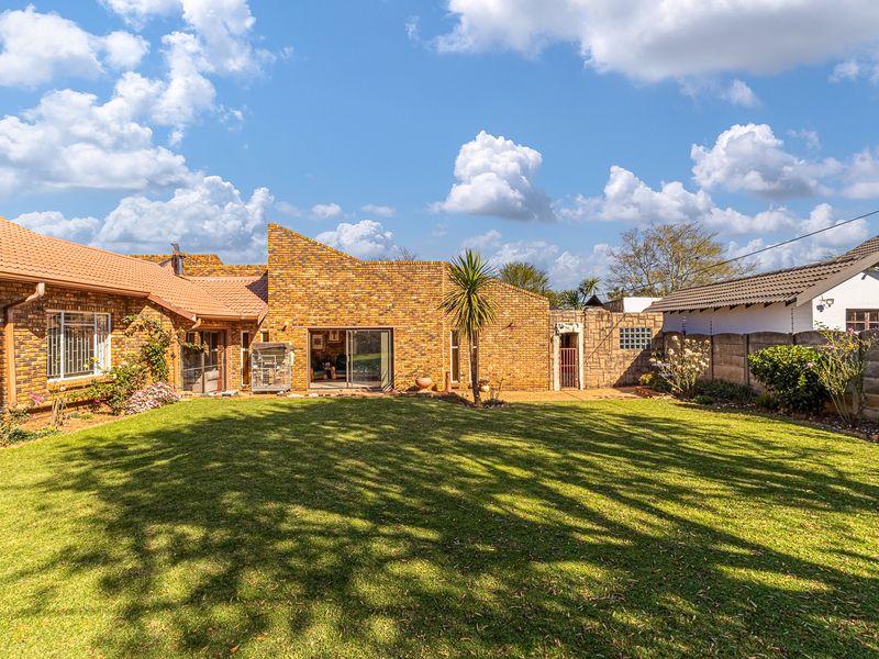 A spacious rear garden featuring a well-maintained lawn, established landscaping, and a face-brick exterior facade with sliding glass doors leading to the interior.