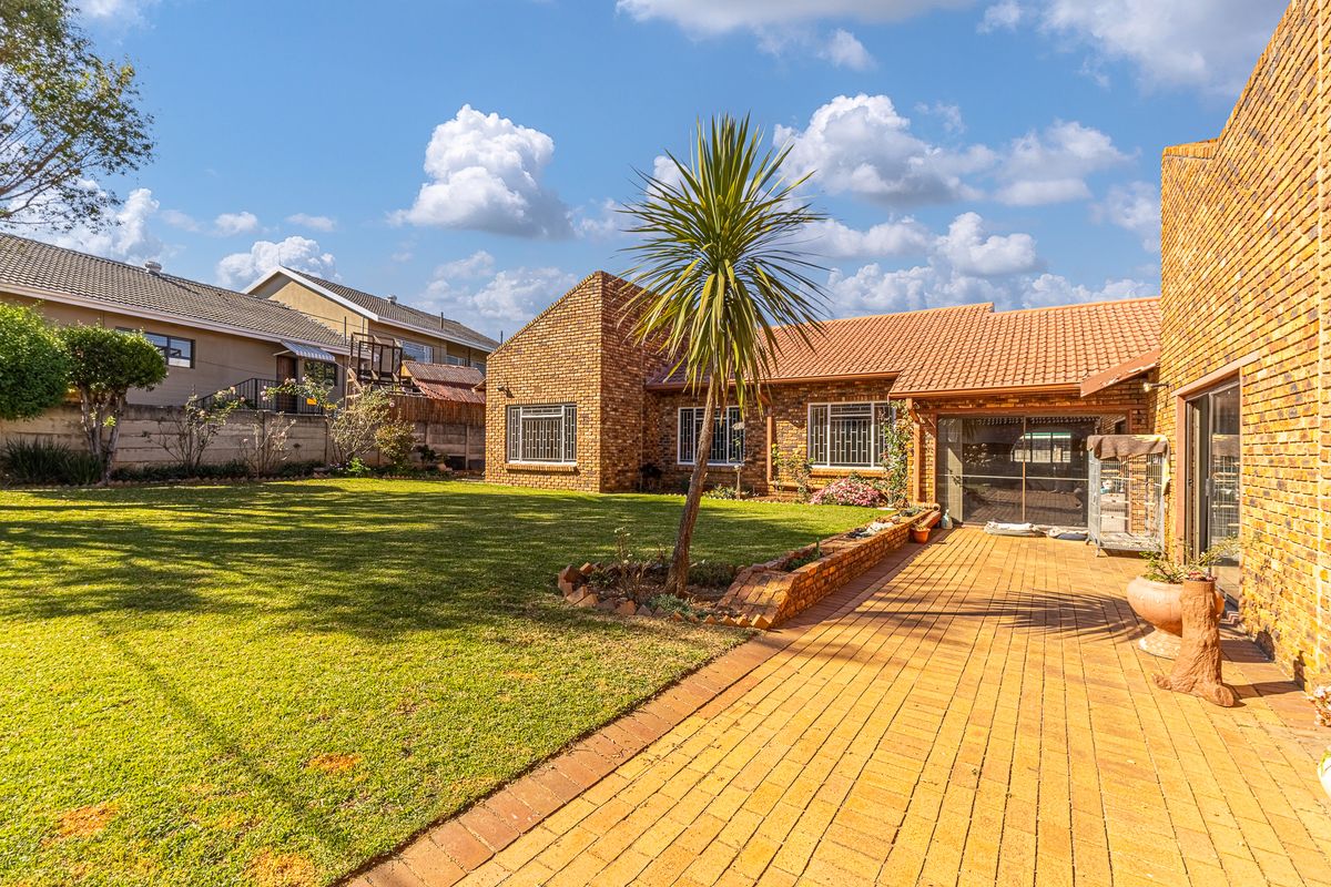 A spacious rear garden featuring a paved patio area, established lawn, and face-brick exterior facade with tiled roofing.