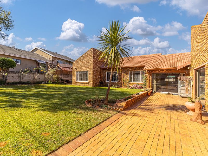A spacious rear garden featuring a paved patio area, established lawn, and face-brick exterior facade with tiled roofing.