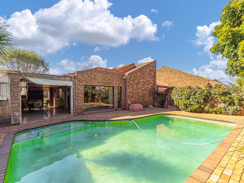 Rear exterior view featuring a swimming pool, brick-paved surround, and a covered patio area attached to the face-brick residence.