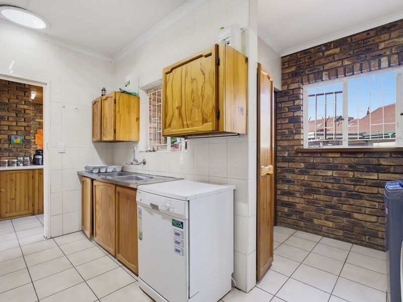 A functional laundry area featuring tiled walls and floors, exposed brick accents, and built-in wooden cabinetry with a stainless steel sink.