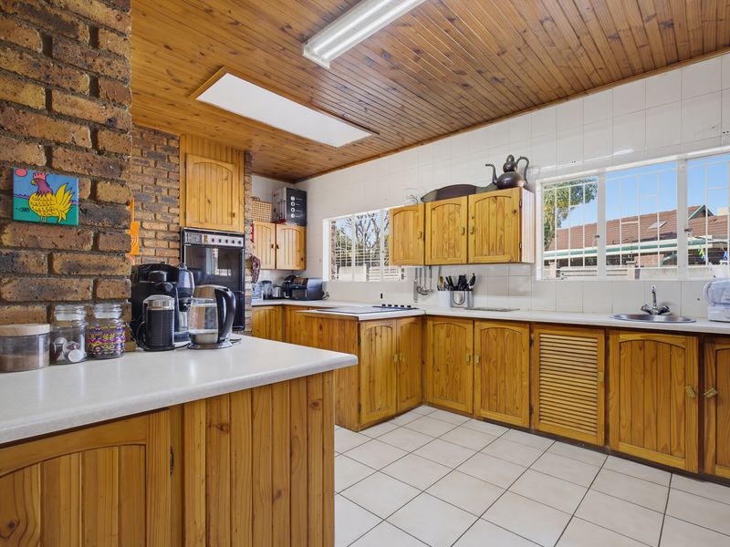 A traditional kitchen featuring timber cabinetry, exposed brickwork, tiled flooring, and a timber-paneled ceiling with integrated lighting.