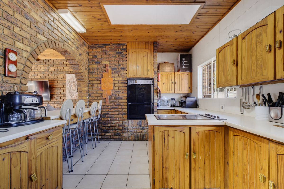 A rustic kitchen featuring exposed brick walls, timber cabinetry, a built-in oven, and a breakfast bar area with tiled flooring.
