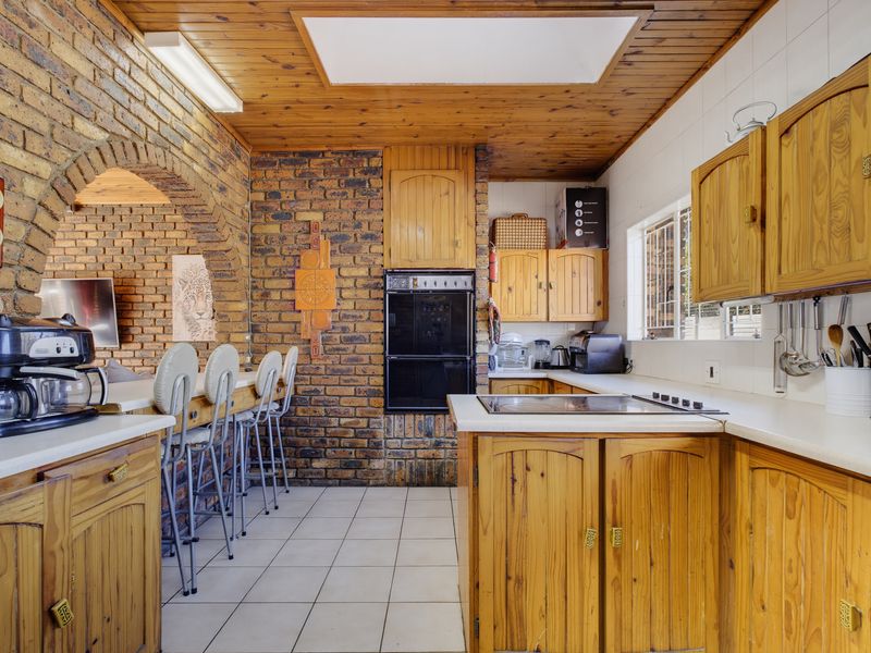 A rustic kitchen featuring exposed brick walls, timber cabinetry, a built-in oven, and a breakfast bar area with tiled flooring.
