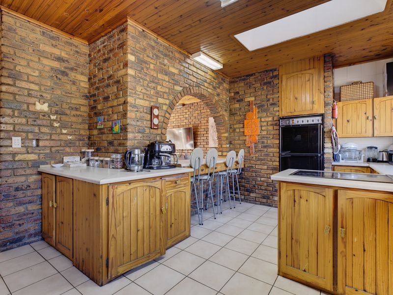 A rustic kitchen featuring exposed brick walls, timber cabinetry, a built-in oven, and a breakfast bar with an arched brick opening.