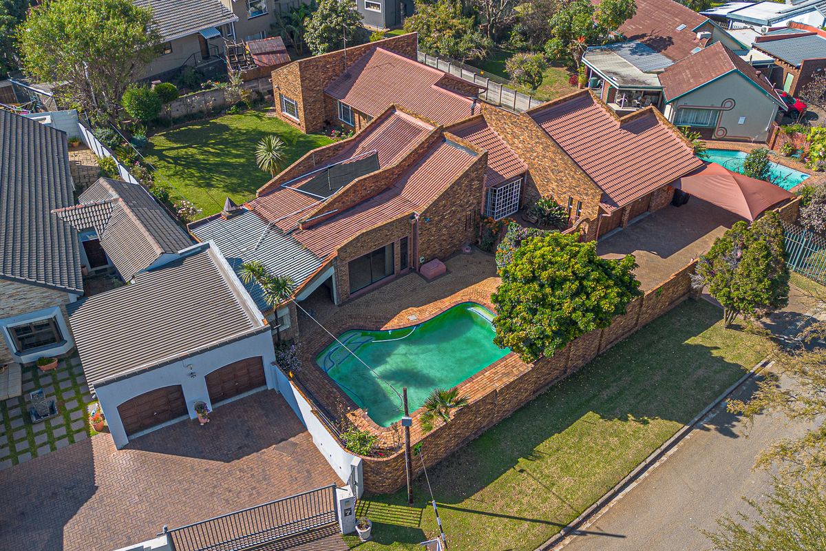 Aerial view of a residential property featuring a brick facade, tiled roof, swimming pool, paved driveway, and a spacious garden area.