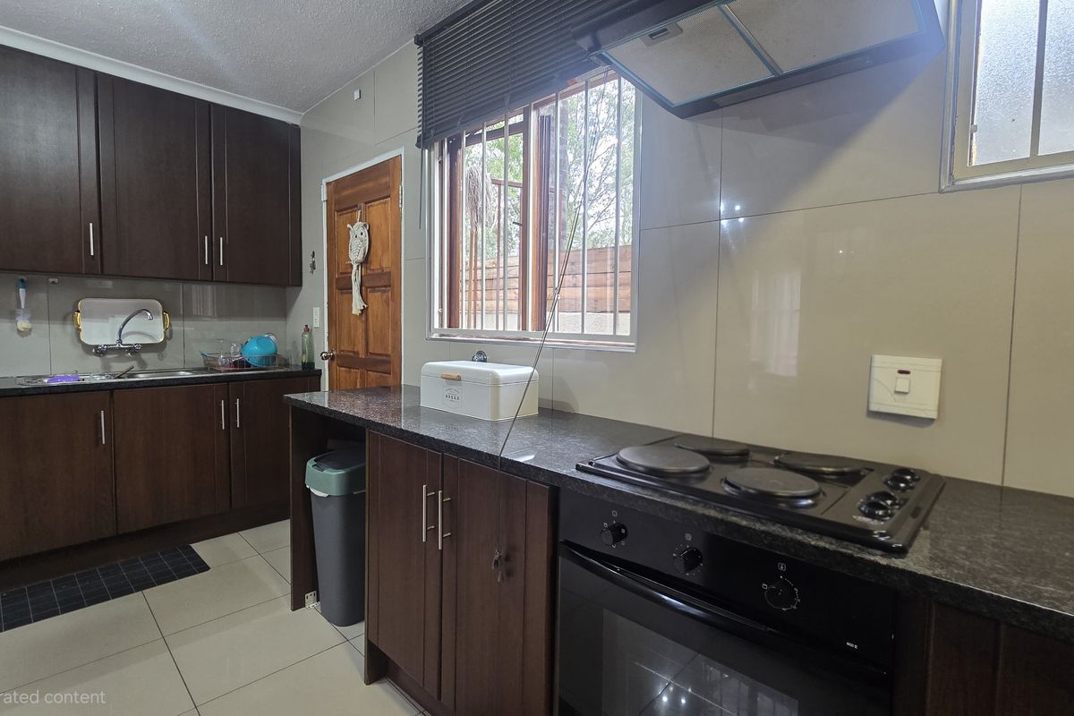A functional kitchen featuring dark wood cabinetry, granite countertops, built-in oven and hob, and tiled splashbacks with a window overlooking the exterior.