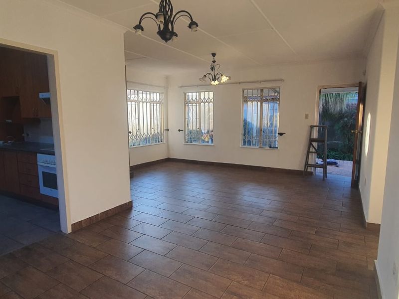 An open-plan living area featuring tiled floors, security bars on windows, and an adjacent kitchen with built-in cabinetry and oven.