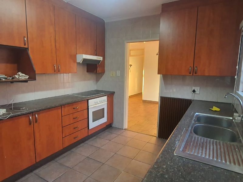 A functional kitchen featuring wood-look cabinetry, laminate countertops, a built-in oven with hob, and a double stainless steel sink.
