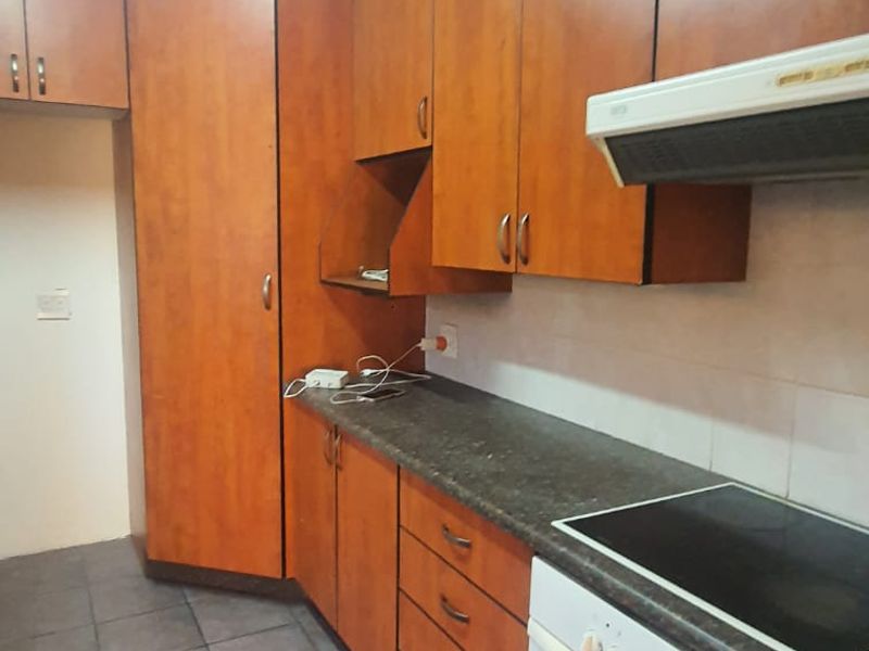 A functional kitchen featuring wood-tone cabinetry, dark laminate countertops, tiled flooring, and integrated cooking appliances including an oven and hob.