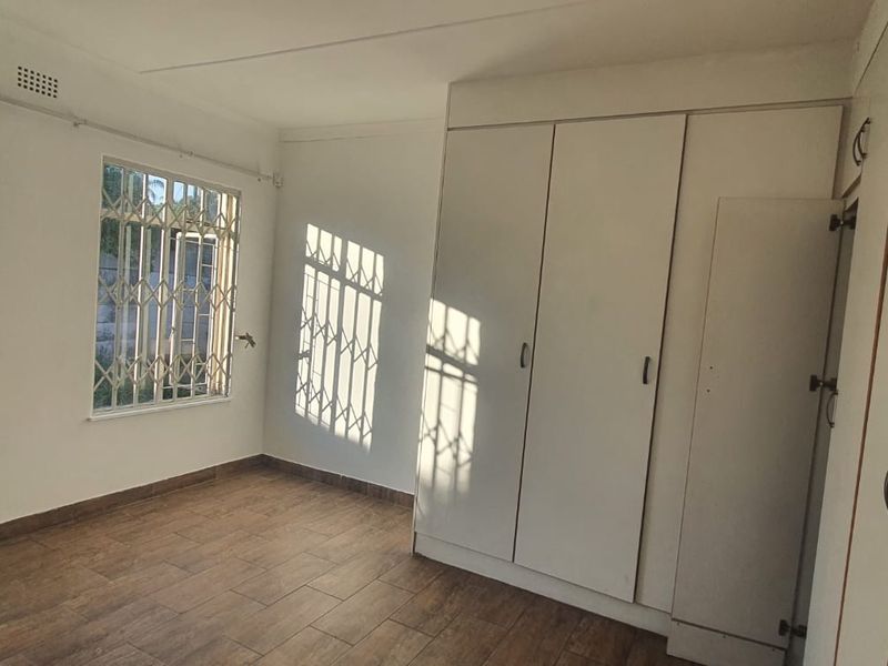 A bright, empty bedroom featuring tiled flooring, built-in cupboards, and security bars on the windows.