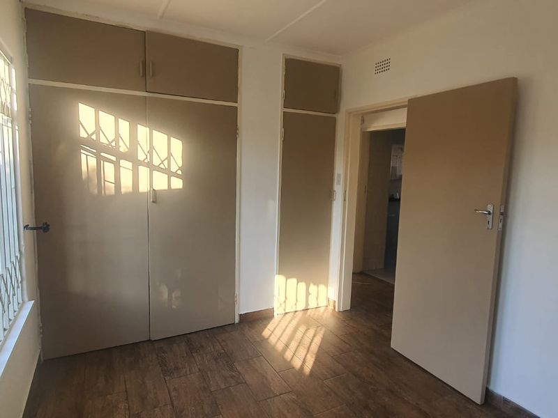 A bright, empty bedroom featuring tiled flooring, built-in cupboards with overhead storage, and security bars on the window.