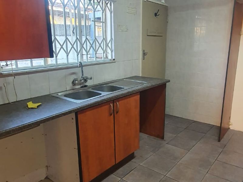 A functional kitchen space featuring tiled flooring, wall tiling, and built-in cabinetry with a double basin sink and window security gate.