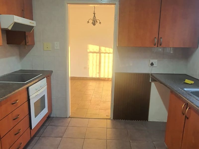 A functional kitchen featuring built-in wooden cabinetry, laminate countertops, an integrated oven and hob, and tiled flooring throughout.