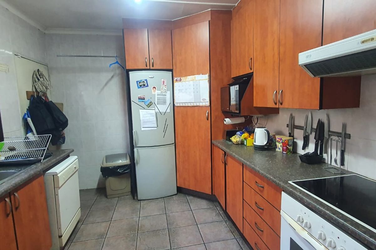 A functional kitchen featuring wood-look cabinetry, laminate countertops, a built-in oven, hob, and extractor fan with tiled splashbacks and flooring.