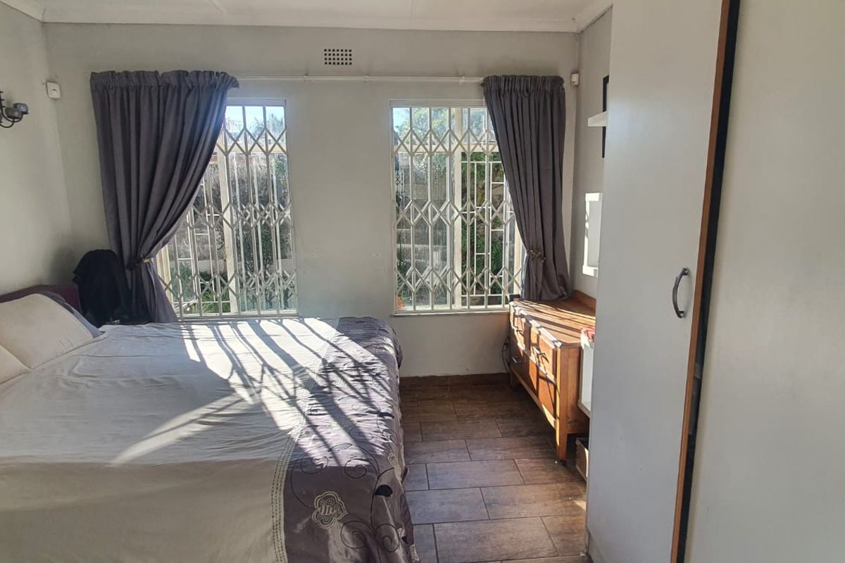 A bedroom featuring tiled flooring, built-in cupboards, and security bars on the windows, providing a functional and secure living space.