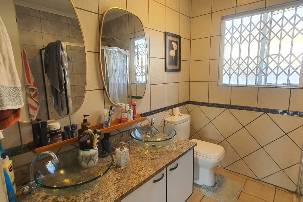 A functional bathroom featuring a double vanity with glass vessel sinks, granite countertop, and a shower enclosure with security bars on the window.