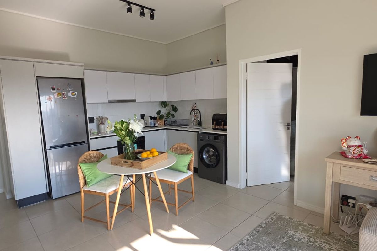 Open-plan kitchen and living area featuring modern white cabinetry, integrated appliances, tiled flooring, and a functional layout suitable for contemporary townhouse living.