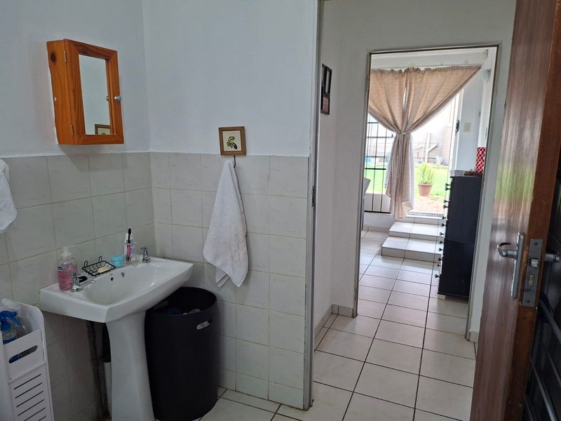 A functional bathroom featuring a pedestal washbasin, tiled walls, and ceramic flooring, with a doorway leading to an outdoor area.