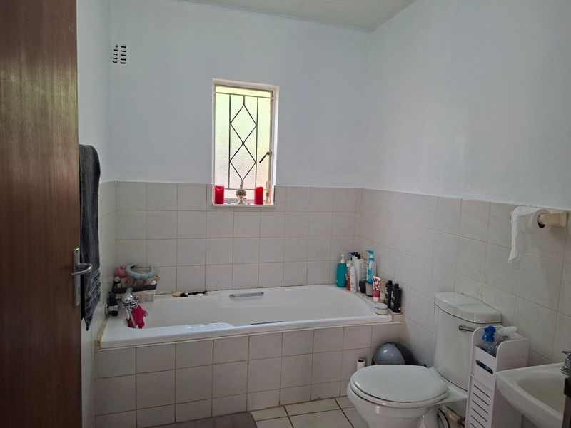 A functional bathroom featuring a built-in bathtub, toilet, and wall-mounted basin with tiled splashbacks and security bars on the window.