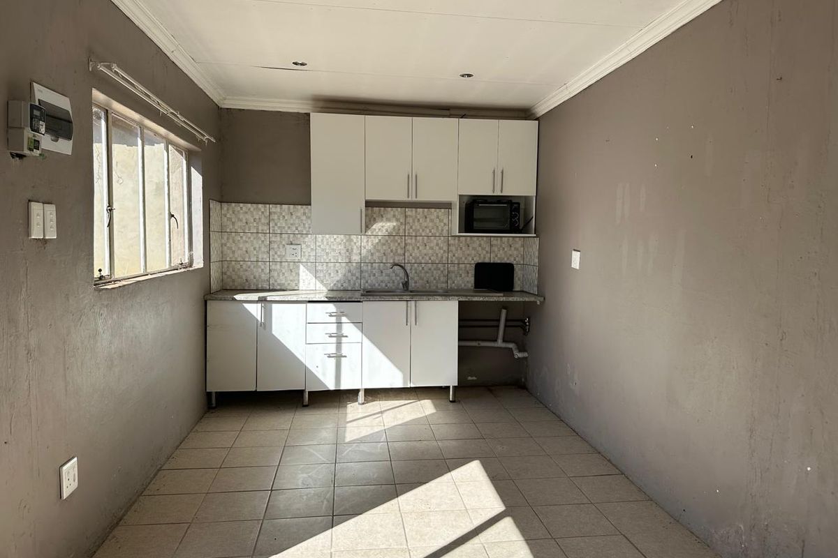 A compact, empty kitchen featuring white cabinetry, tiled backsplash, and tiled flooring, requiring cosmetic updates and minor repairs to the ceiling and plumbing.