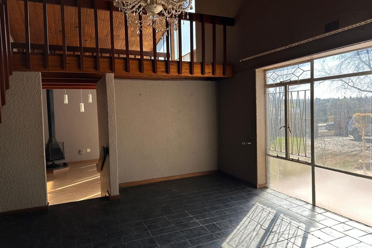 Spacious living area featuring a mezzanine level, vaulted ceilings, a freestanding fireplace, and large windows providing ample natural light.