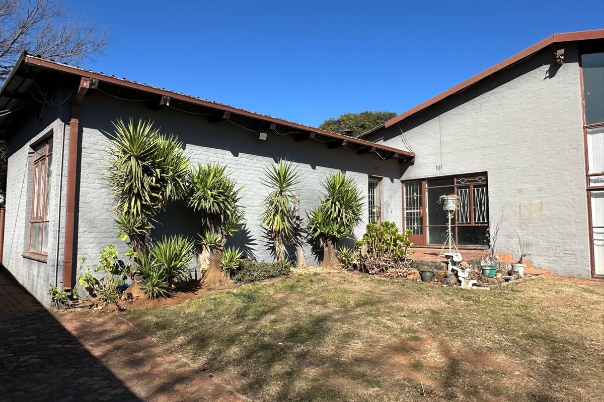 Rear view of the property featuring a brick facade, paved patio area, and established garden space.