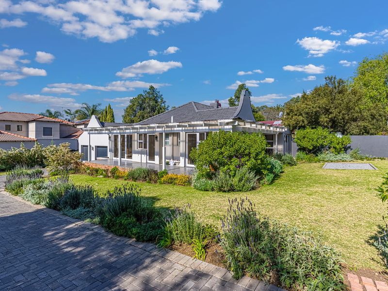 Rear view of the house featuring a spacious landscaped garden, a paved patio area with a pergola, and well-maintained exterior finishes.