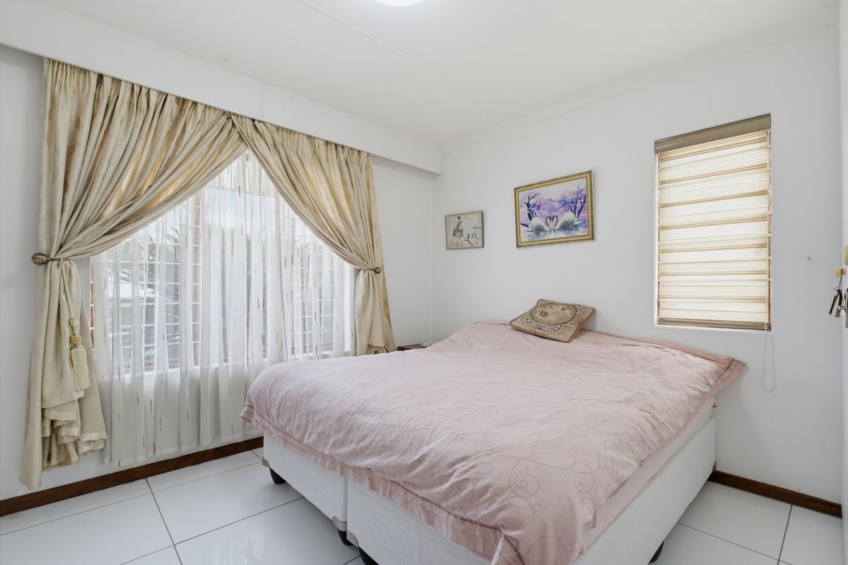 A bright bedroom featuring white tiled flooring, large windows with curtain rails, and fitted roller blinds, offering a clean and functional living space.