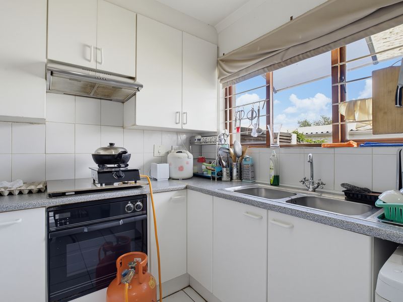 A functional kitchen featuring white cabinetry, a double bowl stainless steel sink, built-in oven, and extractor fan with tiled backsplash and window access.