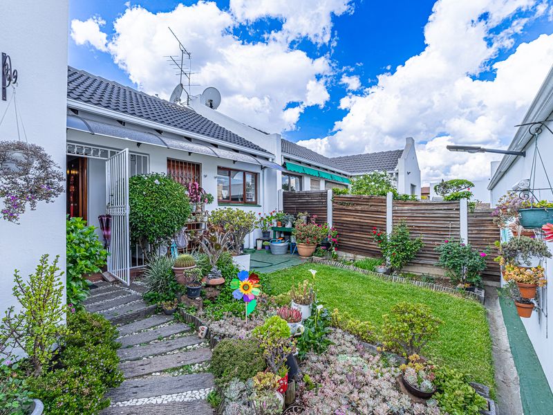 A well-maintained rear garden featuring a lawn, landscaped beds, timber fencing, and a paved pathway leading to the home entrance.