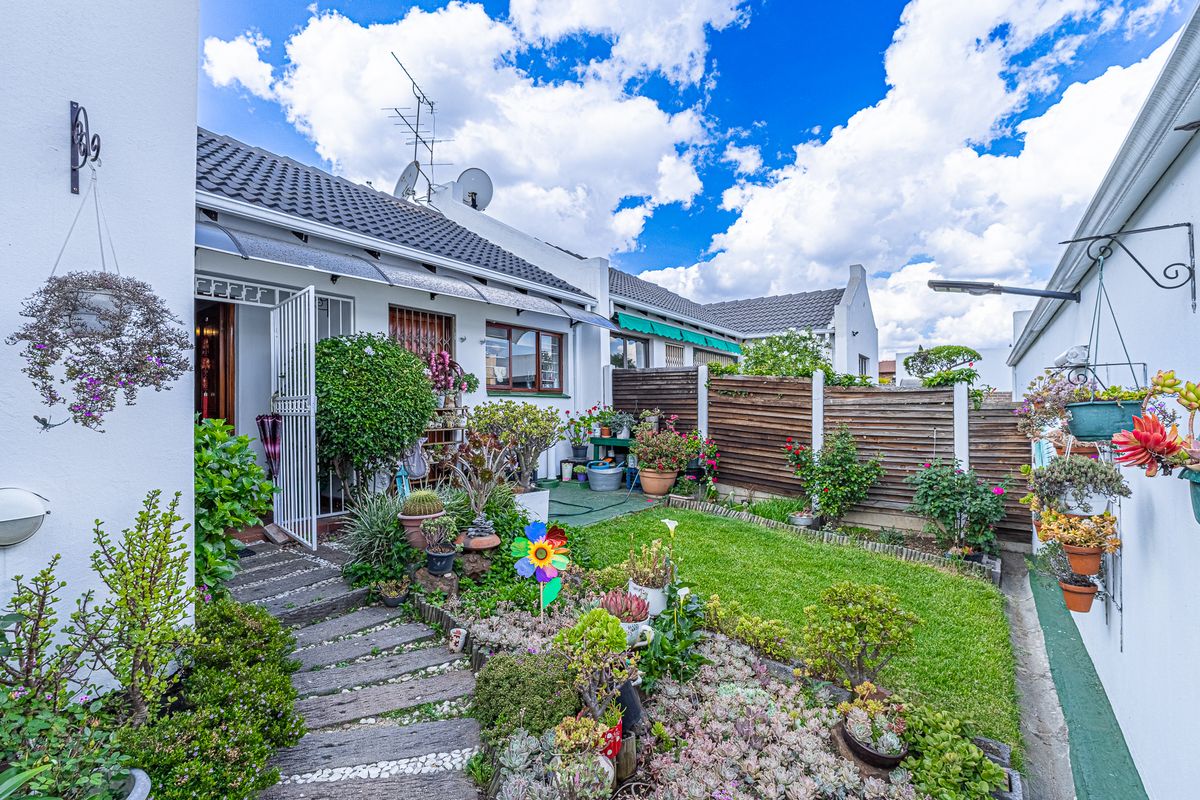 A well-maintained rear garden featuring a lawn, landscaped beds, timber fencing, and a paved pathway leading to the home entrance.