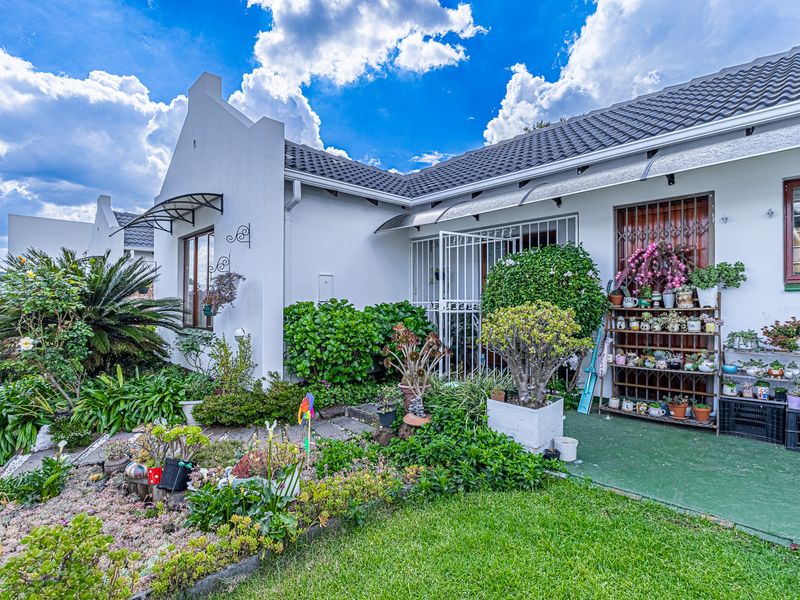 A well-maintained rear exterior view of the house featuring a paved patio area, security fixtures, and established garden landscaping.