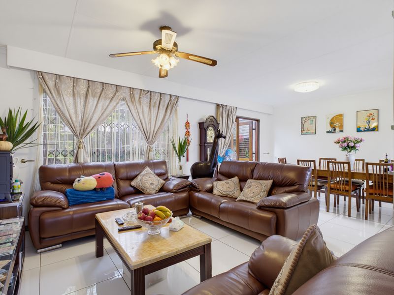Spacious open-plan living and dining area featuring tiled flooring, a ceiling fan, and large windows with security bars.