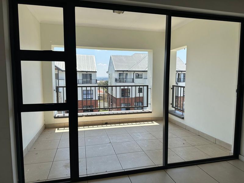 A spacious, covered balcony featuring tiled flooring and a metal balustrade, offering an open-air space accessible through large sliding glass doors.