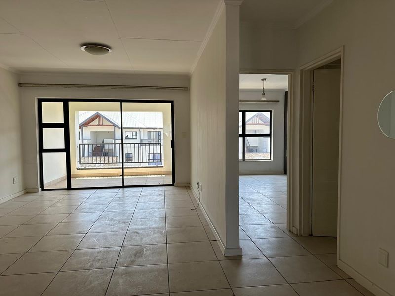 An open-plan living area featuring neutral tiled flooring, a sliding glass door leading to a balcony, and direct access to an adjacent room.