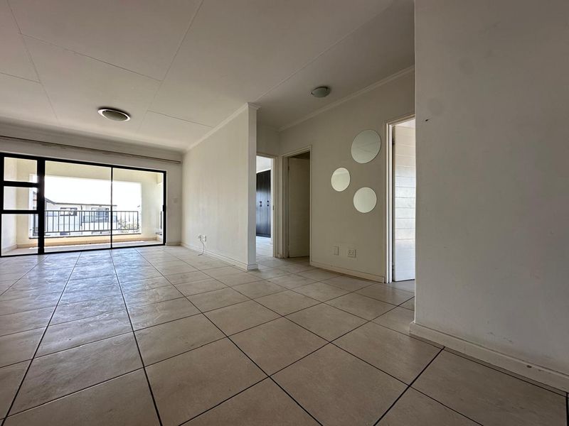 Spacious, open-plan living area featuring neutral tiled flooring and large sliding glass doors that provide access to a private balcony.