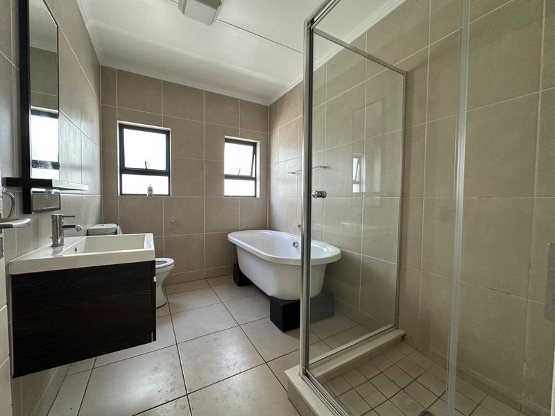 A well-maintained bathroom featuring a freestanding bathtub, a separate glass-enclosed shower, a modern vanity unit, and neutral floor-to-ceiling wall tiling.