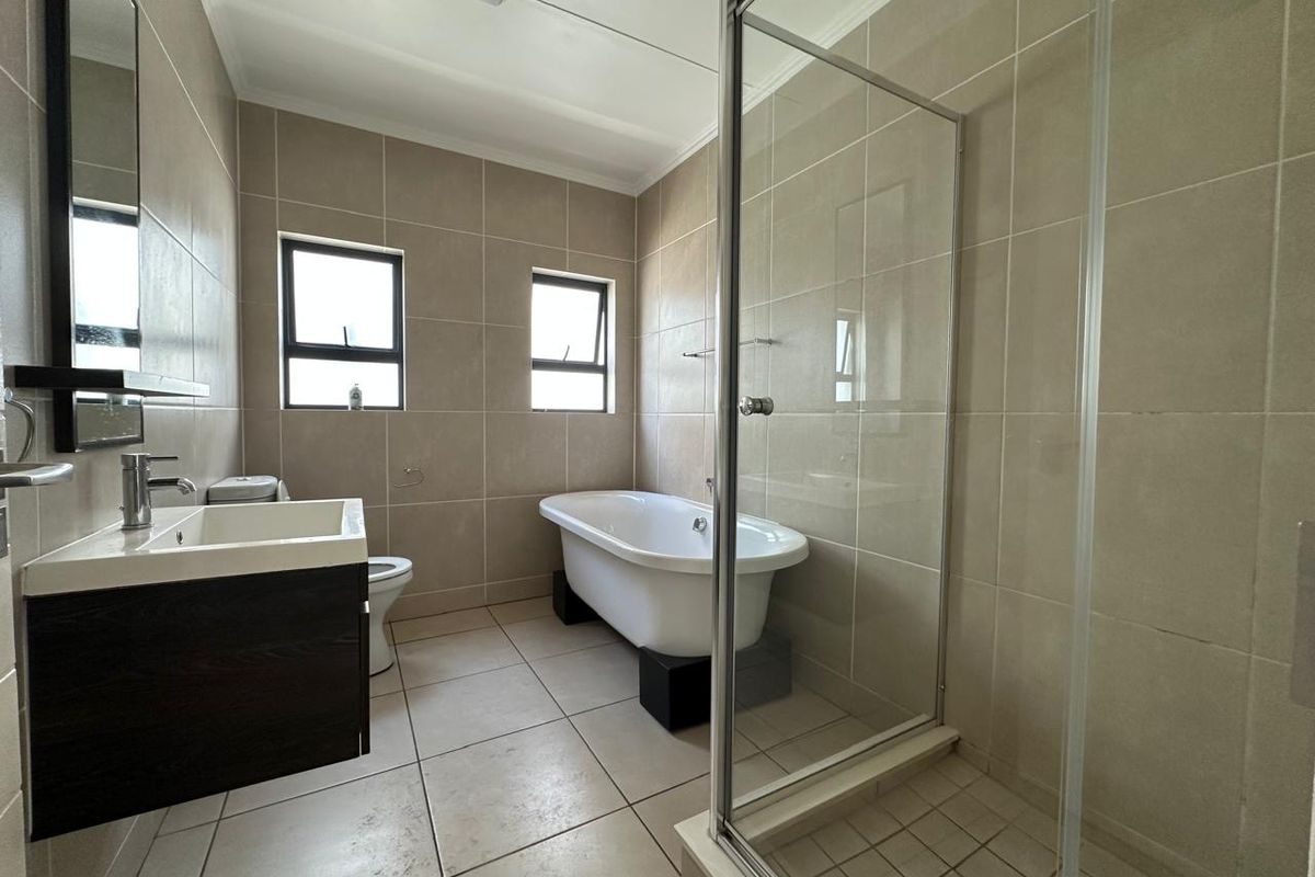 A well-maintained bathroom featuring a freestanding bathtub, a separate glass-enclosed shower, a modern vanity unit, and neutral floor-to-ceiling wall tiling.