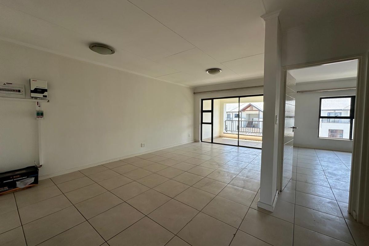 Spacious, empty living area featuring neutral tiled flooring, an integrated inverter system, and large sliding glass doors leading to an outdoor balcony.
