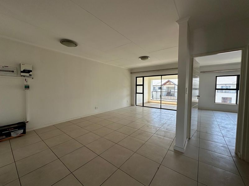 Spacious, empty living area featuring neutral tiled flooring, an integrated inverter system, and large sliding glass doors leading to an outdoor balcony.