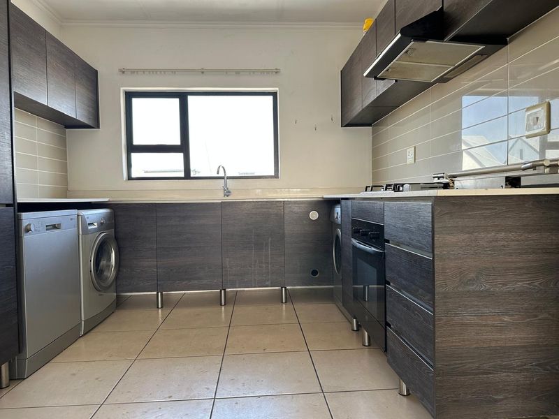 Functional kitchen featuring dark wood cabinetry, tiled backsplash, built-in oven, hob, extractor fan, and tiled flooring with space for under-counter appliances.