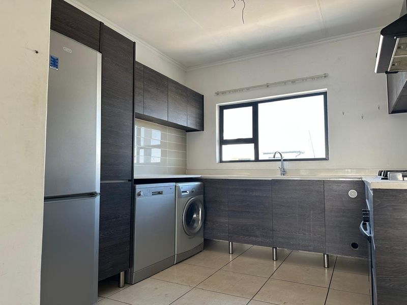 A functional kitchen featuring dark wood-look cabinetry, tiled flooring, a stainless steel sink, and a built-in extractor fan, offering a clean and practical workspace.