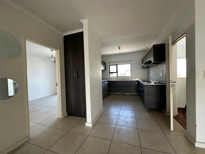 A functional kitchen featuring dark cabinetry, tiled flooring, and integrated cooking appliances, presented in a clean, vacant state ready for personalization.