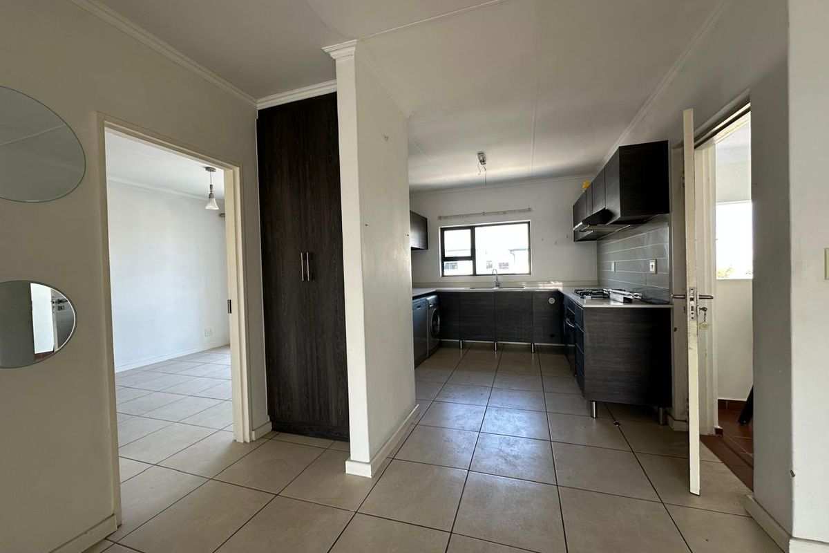 A functional kitchen featuring dark cabinetry, tiled flooring, and integrated cooking appliances, presented in a clean, vacant state ready for personalization.